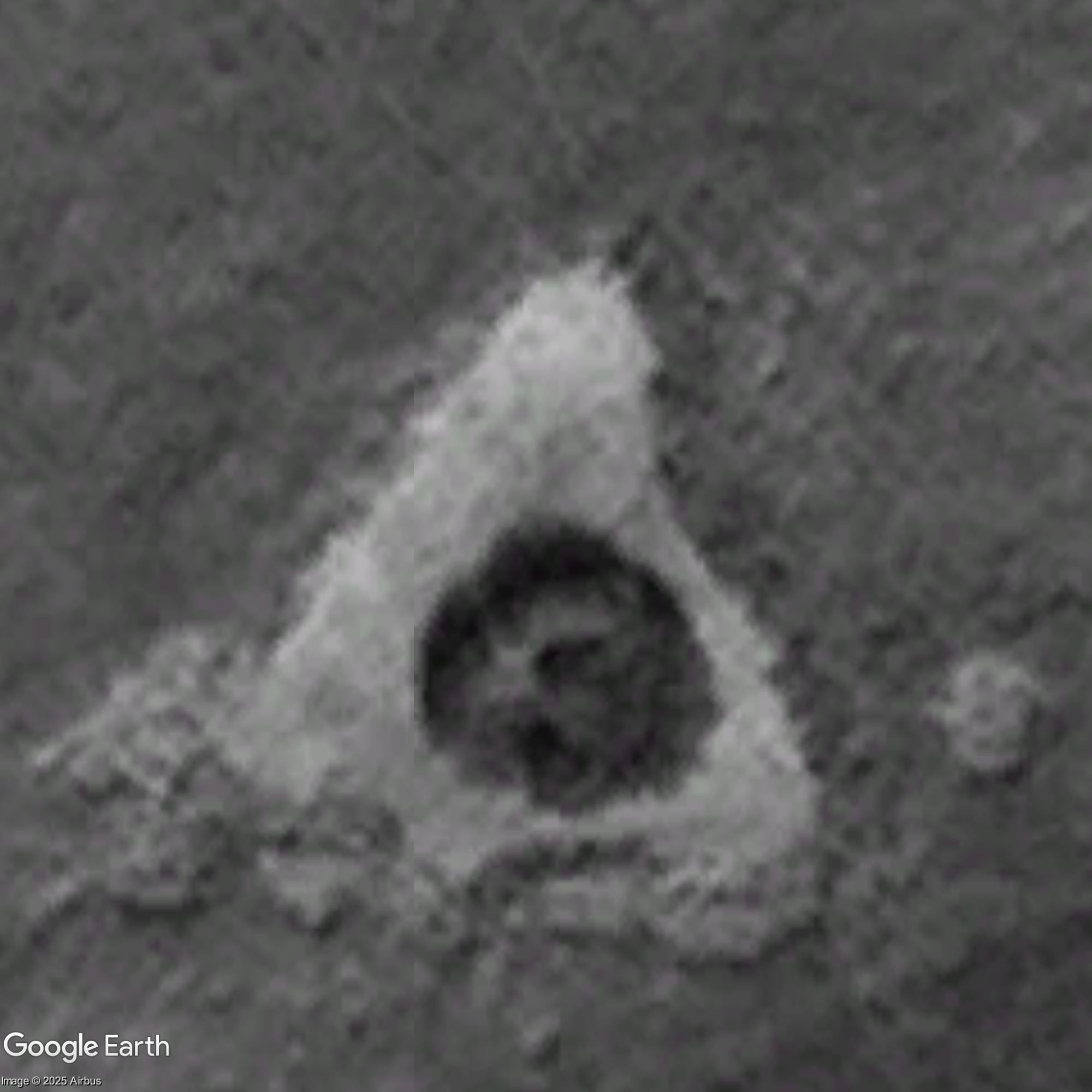 Black-and-white aerial view of the triangular ground feature with central dark form.